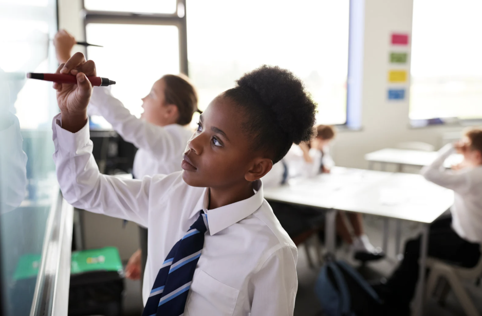 High school student in uniform writes on board.