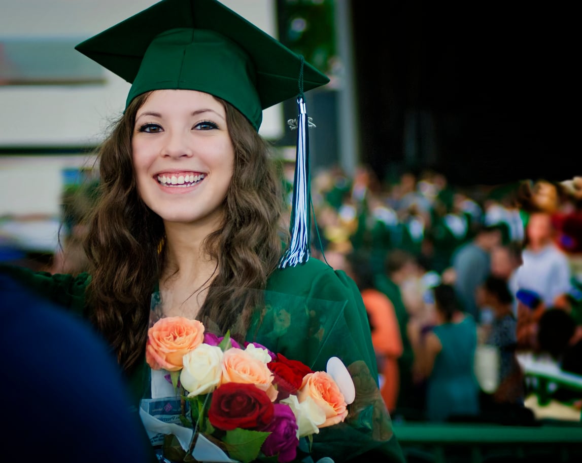 High school graduate girl in cap and gown with roses.