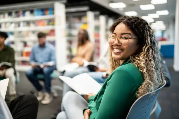 High school student looks at camera with a book in hand in the library.